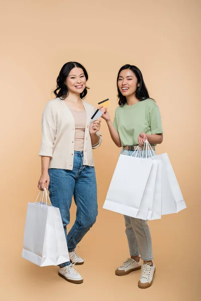 In voller Länge fröhliche asiatische Mutter und Tochter mit Einkaufstaschen und Kreditkarten auf beige — Stockfoto