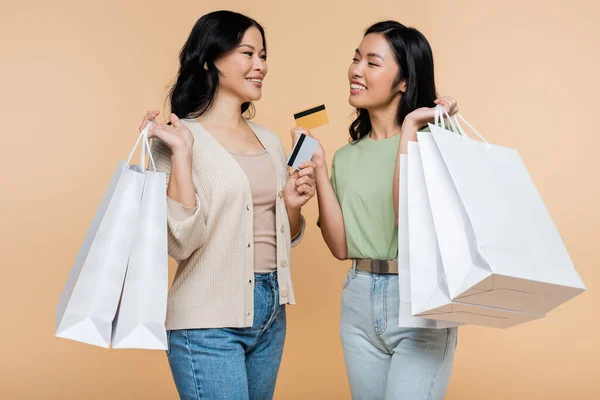 Happy asian mother and daughter with shopping bags and credit cards isolated on beige — Stock Photo