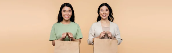 Happy asian mother and daughter with shopping bags isolated on beige, banner — Stock Photo