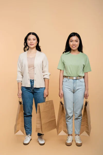 Piena lunghezza di positivo asiatica madre e figlia con sacchetti di carta su beige — Foto stock