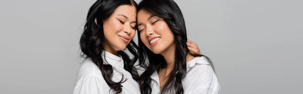 Alegre asiático madre y joven hija en blanco camisas abrazo aislado en gris, bandera - foto de stock