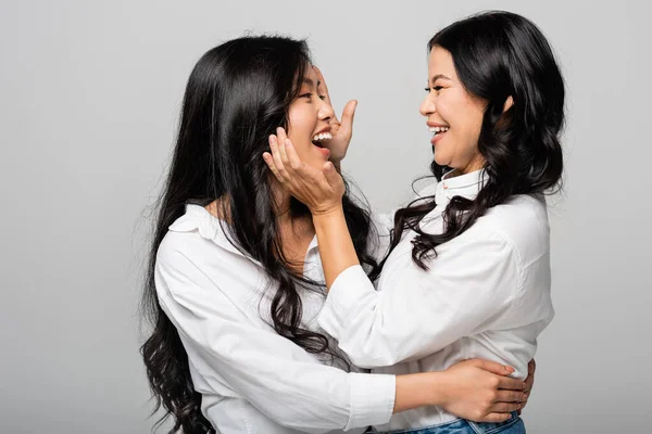 Cheerful asian mother and daughter smiling at each other isolated on grey — Stock Photo