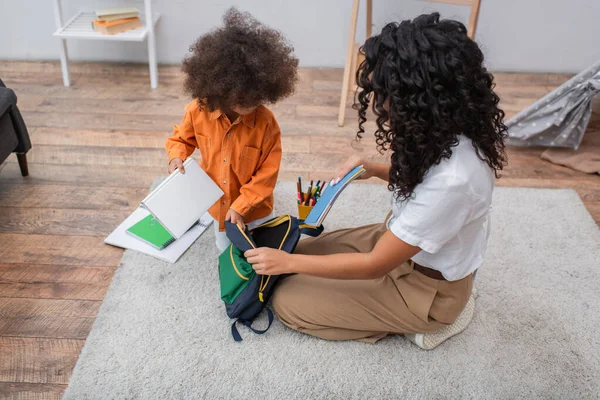 African american kid holding book near mother with backpack at home — Stock Photo