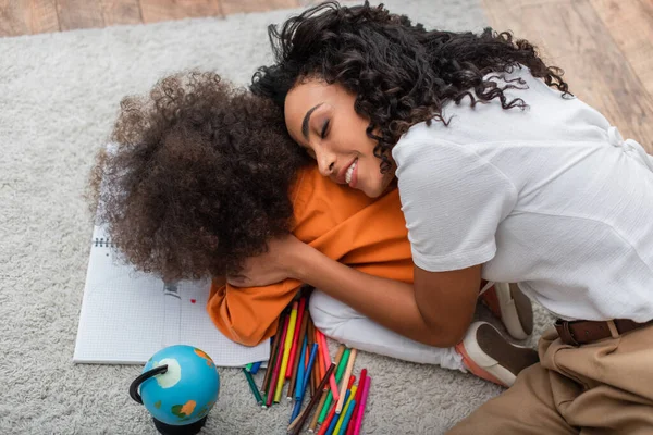 Lächelnde Afroamerikanerin umarmt Tochter in der Nähe von Buntstiften und Globus — Stockfoto