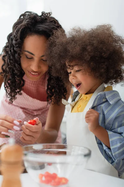 Heureux enfant afro-américain debout près de maman cuisine dans la cuisine — Photo de stock