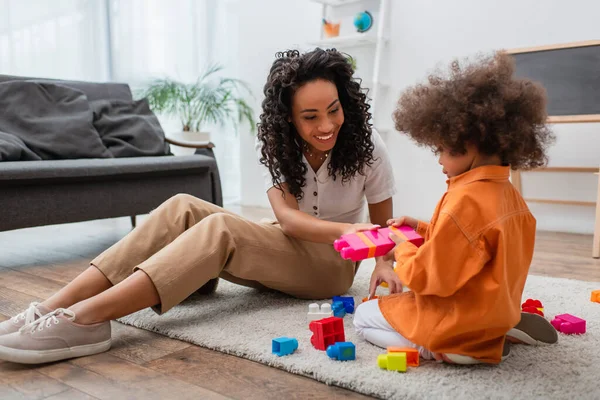 Positivo afro-americano madre seduta vicino figlia giocare mattoni a casa — Foto stock