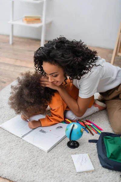 Junge afrikanisch-amerikanische Mutter sitzt neben Tochter und zeichnet zu Hause auf Notizbuch und Globus — Stockfoto