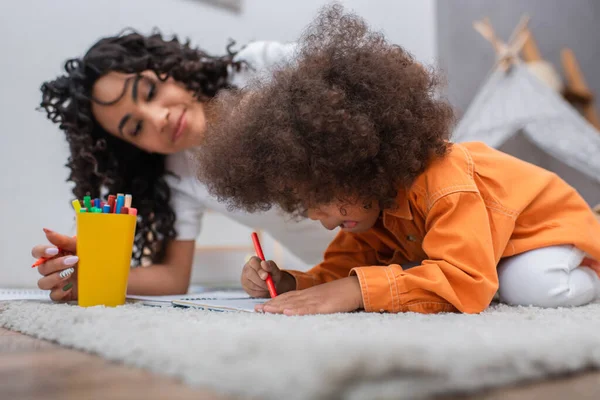 Afroamericano bambino disegno su notebook vicino offuscata mamma a casa — Foto stock