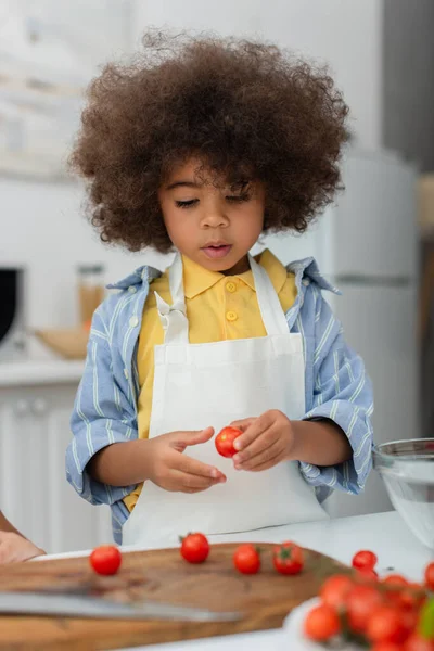 Afrikanisches Kind hält Kirschtomate am Schneidebrett in Küche — Stockfoto