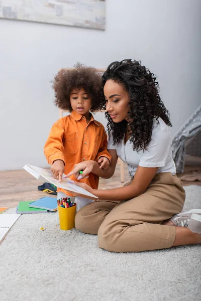 Afroamerikanerin zeigt auf Buch nahe Kleinkind-Tochter zu Hause — Stockfoto