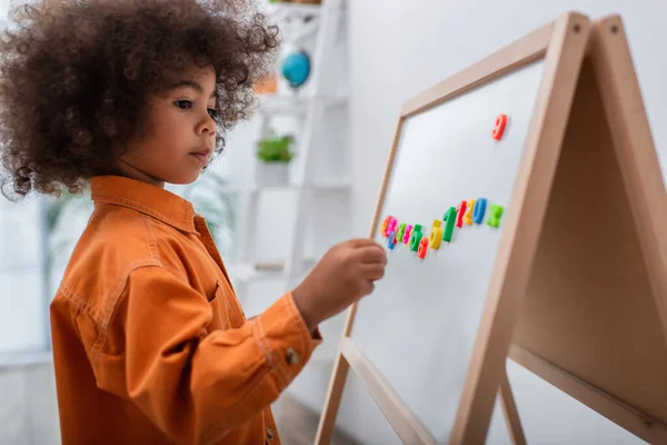 Enfant afro-américain tout-petit debout près du tableau magnétique avec des numéros à la maison — Photo de stock