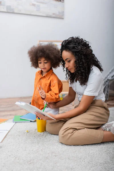 Africano americano mãe segurando livro perto criança e notebook em casa — Fotografia de Stock