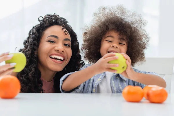 Gai afro-américain femme et enfant tenant des fruits dans la cuisine — Photo de stock