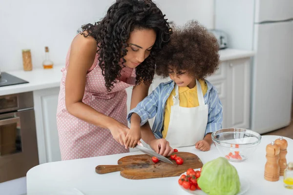 Jovem afro-americana cortando tomates cereja perto da filha e repolho na cozinha — Fotografia de Stock