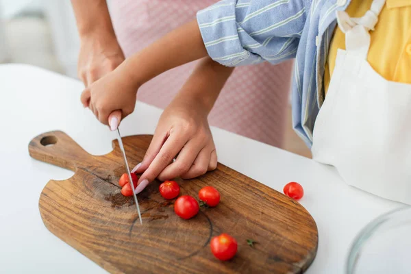 Ausgeschnittene Ansicht eines afrikanisch-amerikanischen Kindes, das die Hand der Mutter hält und in der Küche Kirschtomaten schneidet — Stockfoto