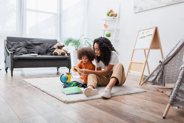 Jeune femme tenant un cahier près de sa fille, sac à dos et globe à la maison — Photo de stock