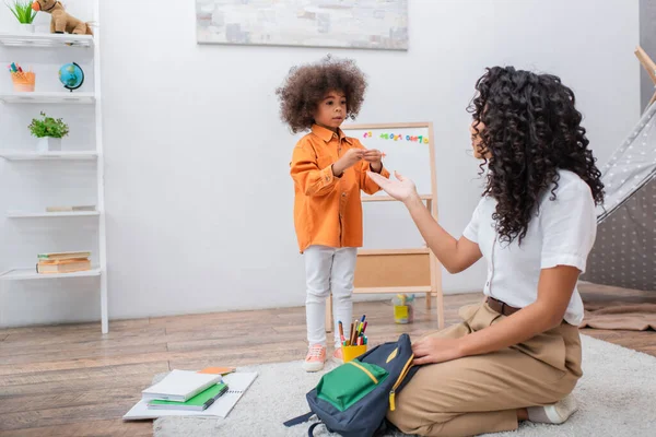 African american kid standing near mother and stationery at home — Stock Photo