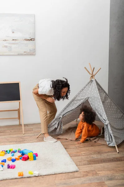 Africano mãe americana olhando para criança criança em teepee em casa — Fotografia de Stock