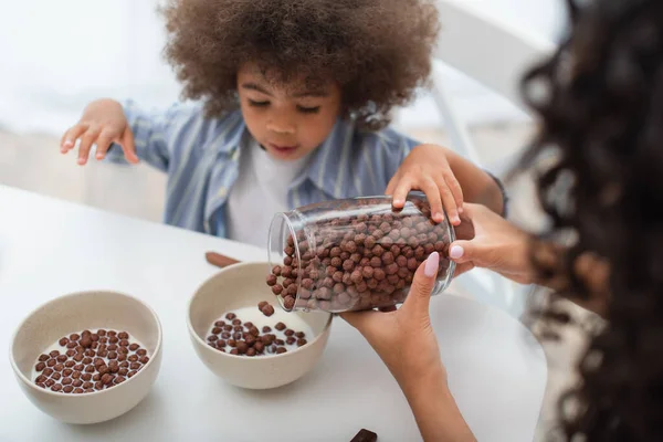 Blurred woman pouring cereal in bowls with milk near african american daughter — Stock Photo