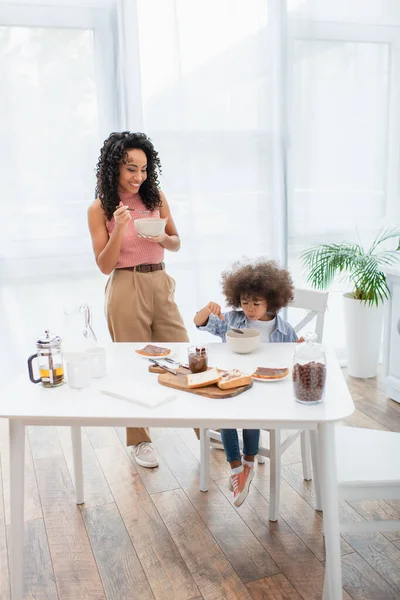 Familia afroamericana desayunando cerca de pasta de chocolate y pan en casa - foto de stock