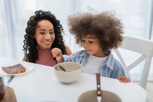 Glückliche Afroamerikanerin schaut Tochter mit Müsli in Küche an — Stockfoto