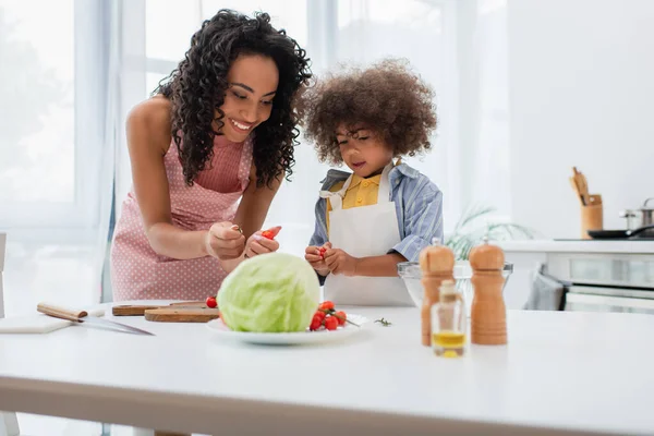 Famiglia afroamericana in grembiuli con pomodorini vicino tagliere in cucina — Foto stock