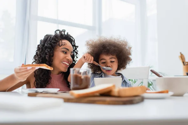 Genitore afroamericano che tiene il pane mentre la figlia mangia cereali a casa — Foto stock