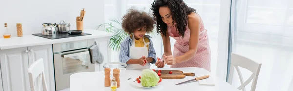 Famiglia afroamericana che tiene pomodorini mentre cucina insalata in cucina, striscione — Foto stock