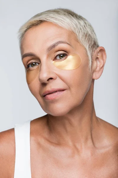 Senior woman with collagen eye patches isolated on grey — Stock Photo