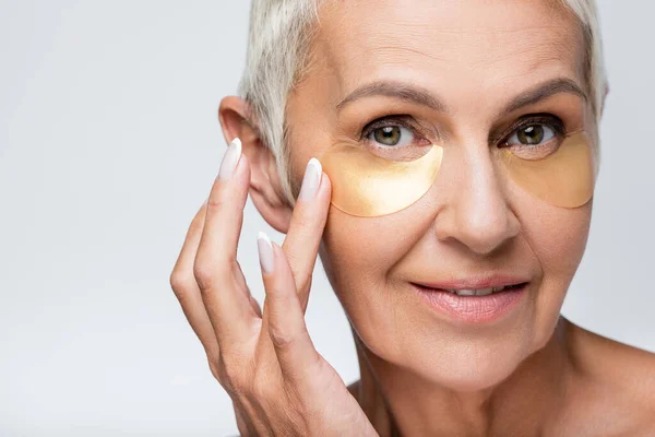 Happy senior woman smiling while applying eye patches isolated on grey — Stock Photo