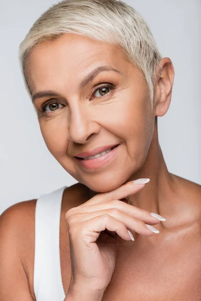 Heureuse femme âgée souriant tout en touchant menton isolé sur gris — Photo de stock