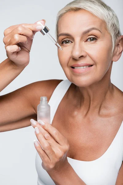 Heureuse femme âgée appliquant sérum avec pipette isolé sur gris — Photo de stock