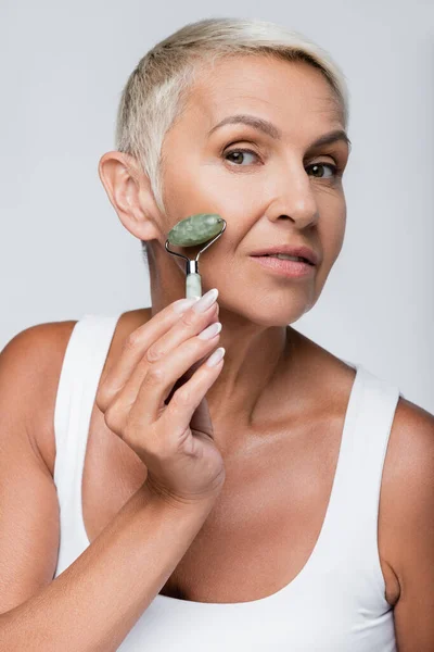 Senior woman massaging face with jade roller isolated on grey — Stock Photo