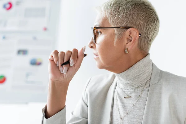 Mujer de negocios pensativa y senior en gafas con pluma - foto de stock