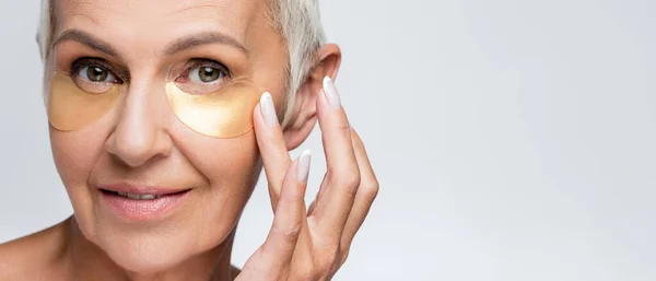 Glückliche Seniorin, die Kollagen-Augenklappen isoliert auf grau aufträgt, Banner — Stockfoto