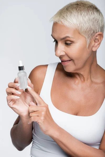 Glückliche Seniorin zeigt auf Flasche mit Serum isoliert auf grau — Stockfoto