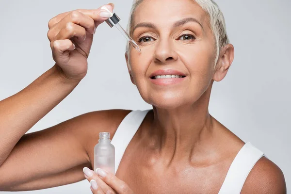 Glückliche Seniorin unter Anwendung von Vitamin-C-Serum isoliert auf grau — Stockfoto