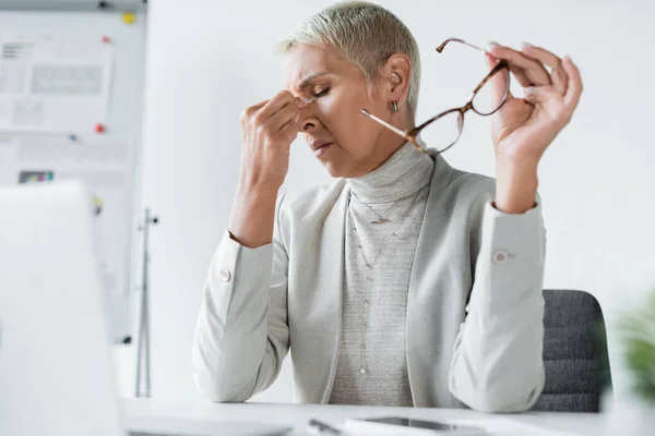 Müde Geschäftsfrau mit grauen Haaren, die Augen berührt und eine Brille hält — Stockfoto