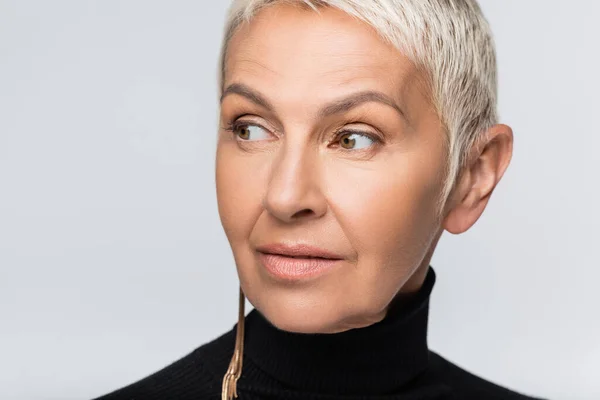 Senior femme avec boucle d'oreille longue et col roulé noir isolé sur gris — Photo de stock