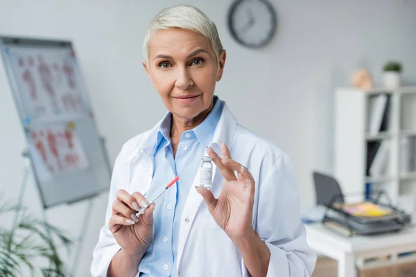 Arzt mit grauen Haaren hält Flasche mit Impfstoff und Spritze in den Händen — Stockfoto