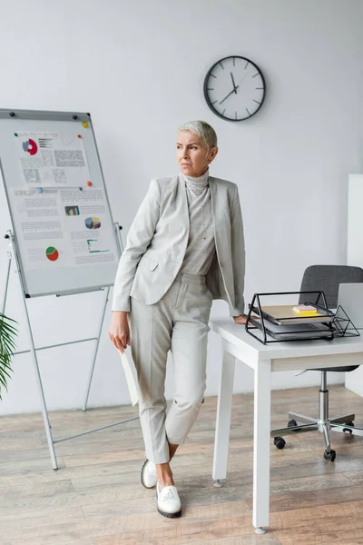 Full length of businesswoman with grey hair standing near desk — Stock Photo