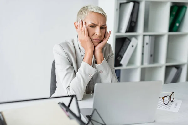 Gelangweilte Seniorin blickt auf Laptop auf Schreibtisch — Stockfoto