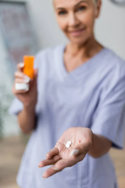 Infirmière souriante et floue tenant des pilules à la main — Photo de stock