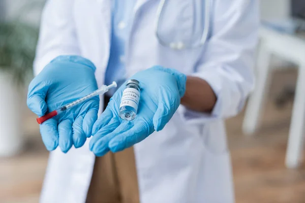 Vista parcial del médico en guantes de látex sosteniendo frasco con vacuna y jeringa en las manos - foto de stock