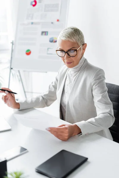 Старша бізнес-леді в окулярах дивиться на документ в офісі — стокове фото