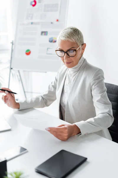 Mujer de negocios senior en gafas mirando documento en la oficina - foto de stock