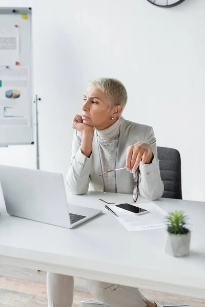 Chère femme d'affaires aux cheveux gris tenant des lunettes sur le lieu de travail — Photo de stock