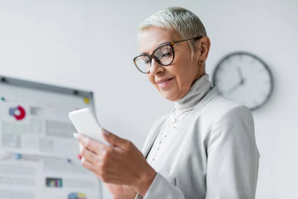 Soddisfatto anziana donna d'affari in occhiali guardando smartphone — Foto stock