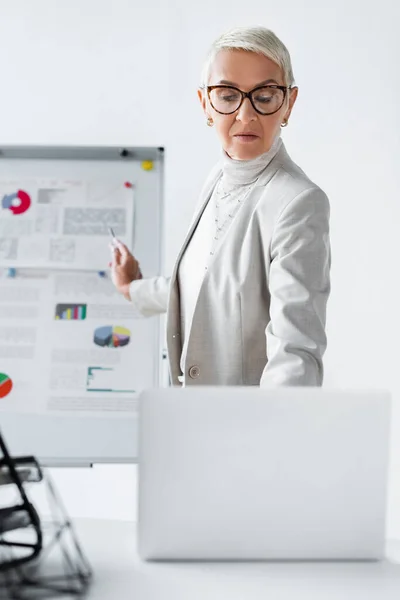 Seniorin mit Brille blickt auf verschwommenen Laptop — Stockfoto