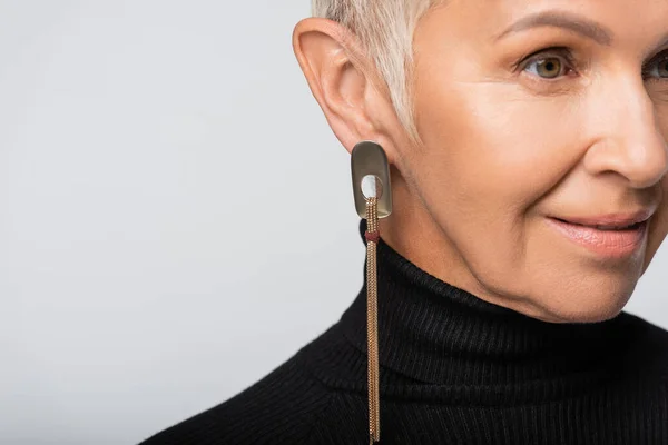 Smiling and senior woman with long earring and black turtleneck looking away isolated on grey — Stock Photo